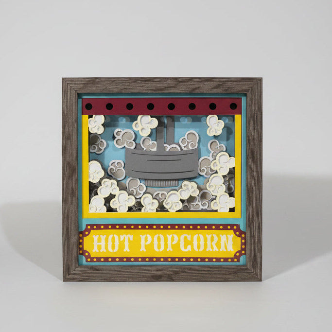Decorative shadow box with popcorn design and 'Hot Popcorn' text on a wall.