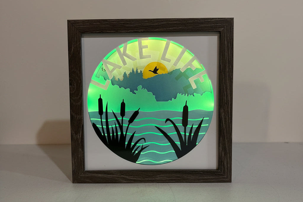 Framed artwork with a circular design of a lake scene on a wall.
