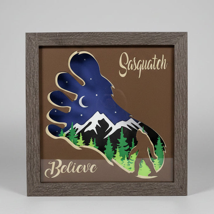 Framed artwork with a foot design and 'Sasquatch Believe' text on a wall.