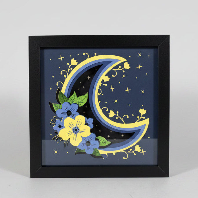 Decorative wall art with floral design and moon on a black frame.